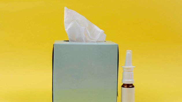 A box of tissues and nasal spray to a yellow background