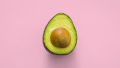 An avocado sliced in half on a pink background